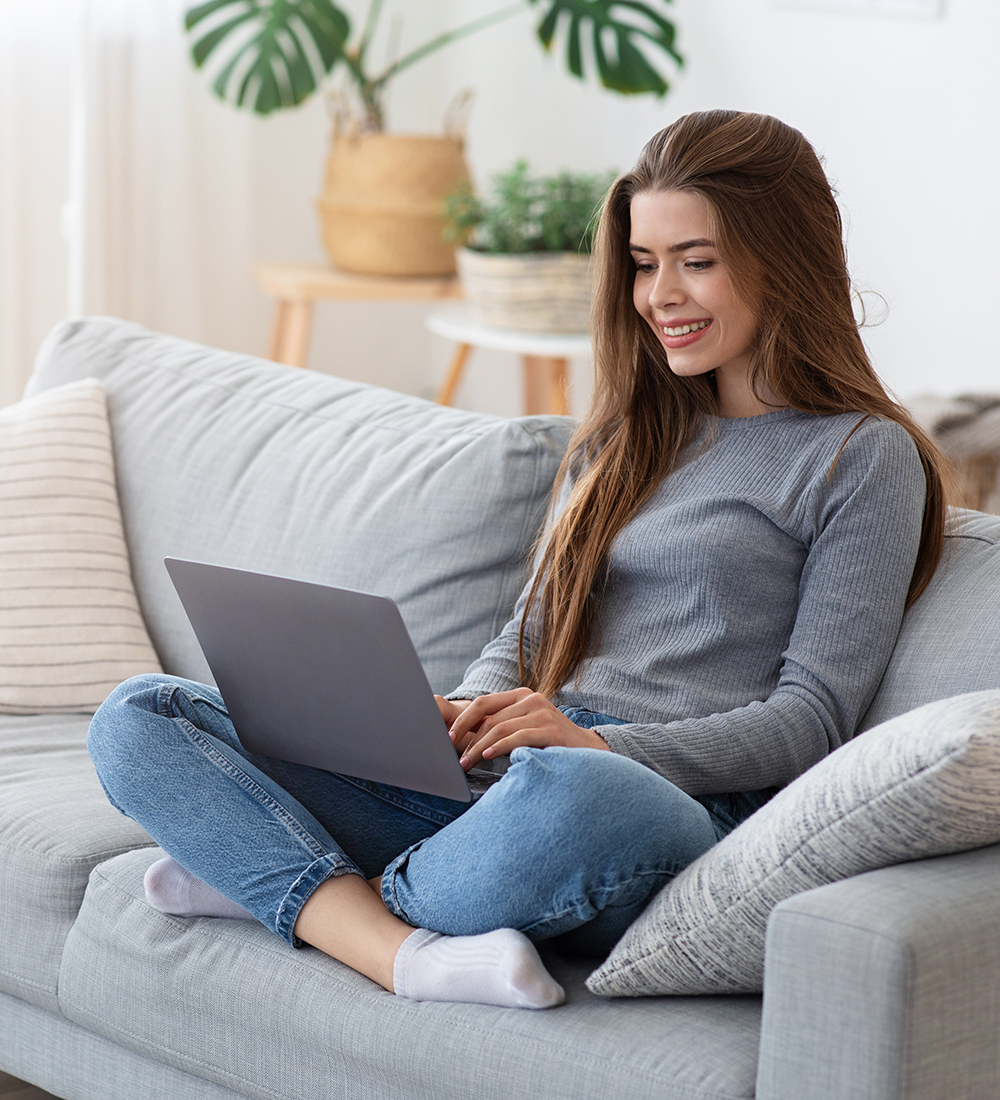 Smiling Young Lady Sitting With Laptop On Couch At Home